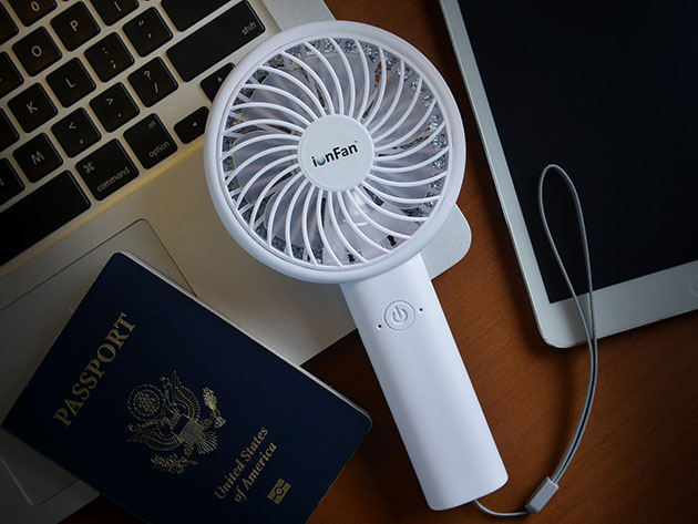 A fan resting on a laptop next to a passport