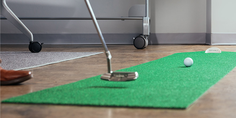 A golf club hitting a ball on a strip of indoor green 